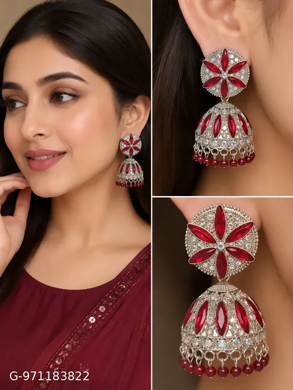 These silver-plated jhumka earrings feature a prominent floral design studded with red stones and smaller shimmering stones.