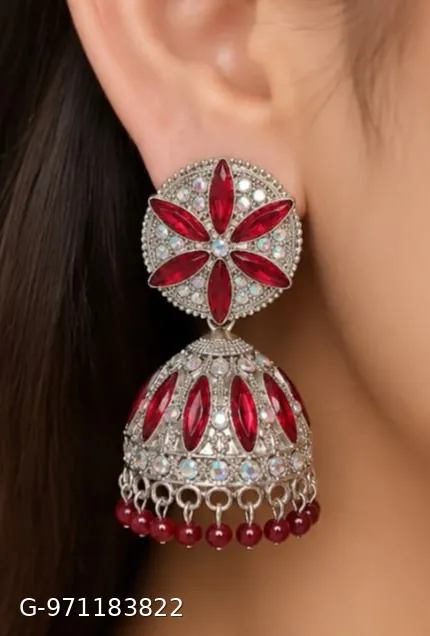 These silver-plated jhumka earrings feature a prominent floral design studded with red stones and smaller shimmering stones.